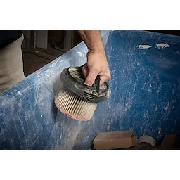 A person holds a dust-covered filter from the M18 FUEL™ 3-in-1 Backpack Vacuum over a blue container, likely for cleaning or replacement.