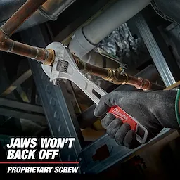 A Milwaukee adjustable wrench grips a metal pipe while held by a hand wearing a black glove. The text "JAWS WON'T BACK OFF PROPRIETARY SCREW" is displayed in the lower left corner.