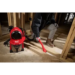 A person uses the M18 FUEL™ 3-in-1 Backpack Vacuum in a construction site, cleaning wooden beams and floors. The vacuum is red with a black and silver finish, and is designed to be carried as a backpack for ease of use in various work environments.
